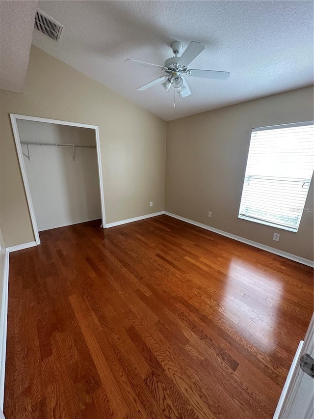 unfurnished bedroom with a textured ceiling, a closet, wood finished floors, and visible vents