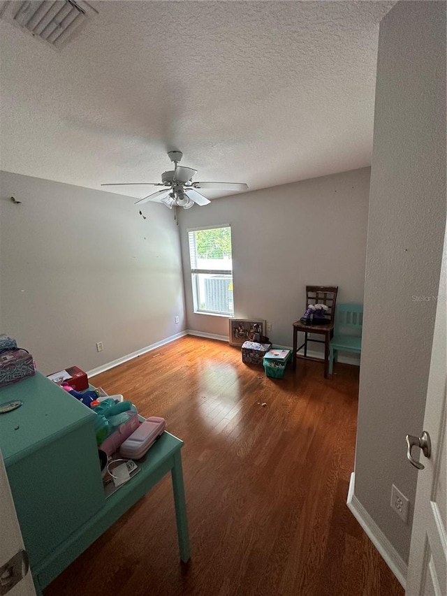 sitting room featuring ceiling fan, a textured ceiling, wood finished floors, visible vents, and baseboards