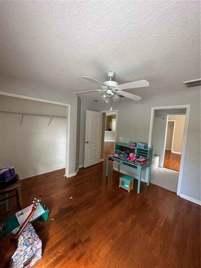 playroom featuring a textured ceiling, ceiling fan, wood finished floors, visible vents, and baseboards