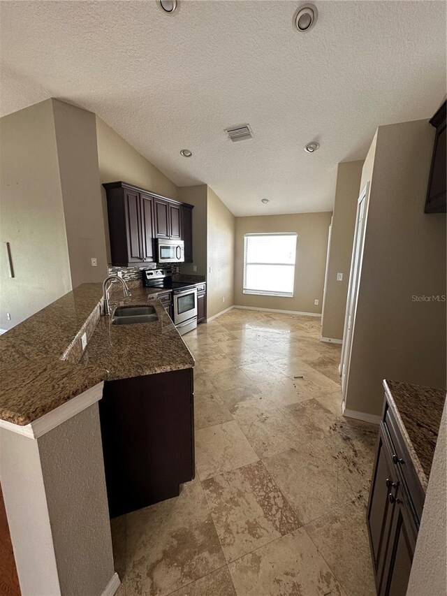 kitchen featuring visible vents, appliances with stainless steel finishes, a sink, dark stone countertops, and baseboards