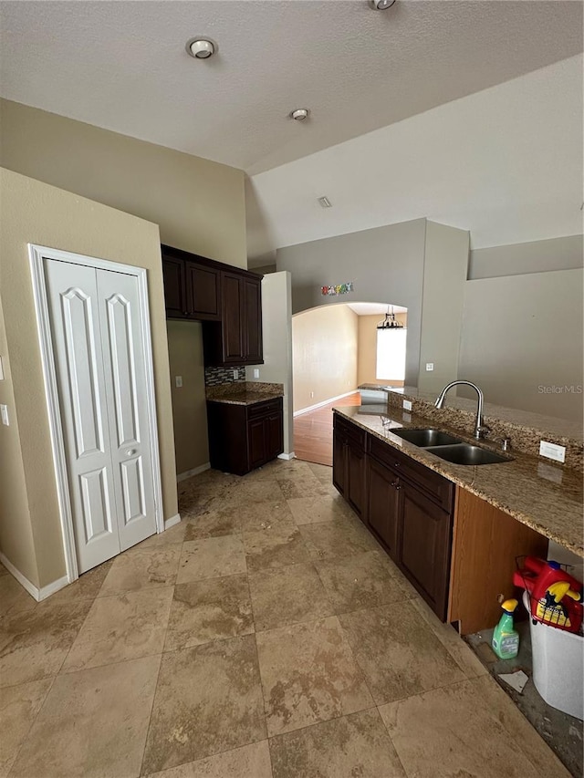 kitchen with vaulted ceiling, baseboards, a sink, and dark brown cabinets