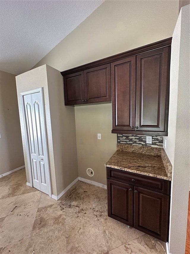 kitchen with baseboards, vaulted ceiling, a textured ceiling, dark brown cabinets, and backsplash