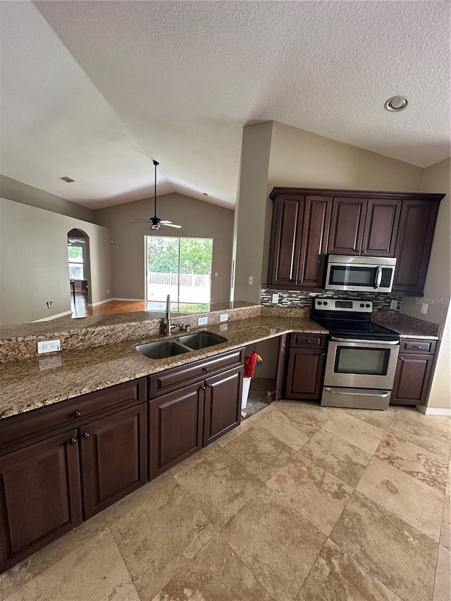 kitchen with dark brown cabinetry, lofted ceiling, dark stone countertops, stainless steel appliances, and a sink