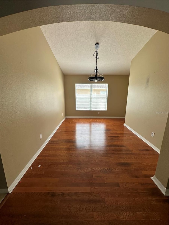 unfurnished dining area featuring a textured ceiling, wood finished floors, and baseboards