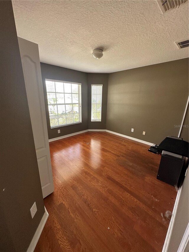 unfurnished room with a textured ceiling, wood finished floors, visible vents, and baseboards