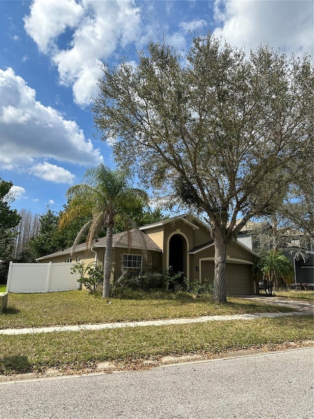 ranch-style house featuring an attached garage, fence, and stucco siding