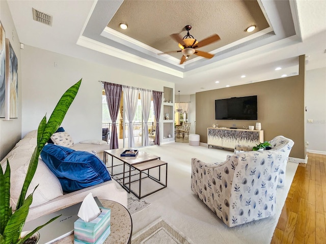 living room featuring a tray ceiling, ceiling fan, light hardwood / wood-style floors, and a textured ceiling