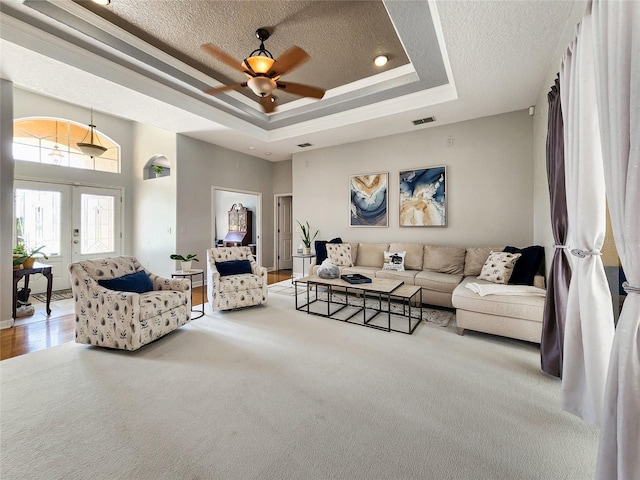 living room featuring a textured ceiling, a raised ceiling, light carpet, french doors, and ceiling fan