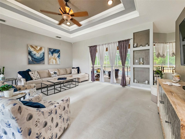 carpeted living room with a wealth of natural light, a raised ceiling, ceiling fan, and ornamental molding