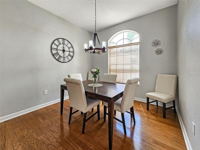 dining space featuring wood-type flooring, a notable chandelier, and a textured ceiling