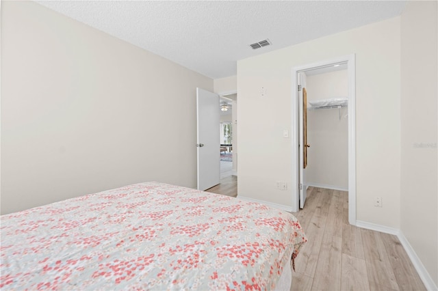 bedroom featuring a walk in closet, a textured ceiling, a closet, and light wood-type flooring