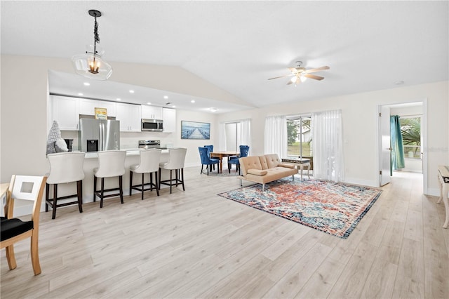 living room with vaulted ceiling, ceiling fan, and light wood-type flooring