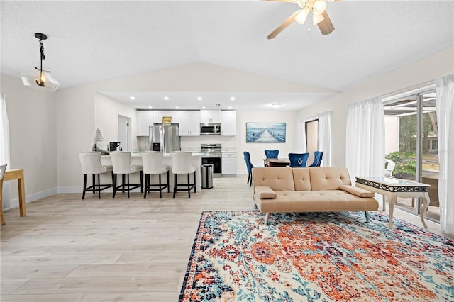 living room featuring a textured ceiling, vaulted ceiling, light hardwood / wood-style floors, and ceiling fan