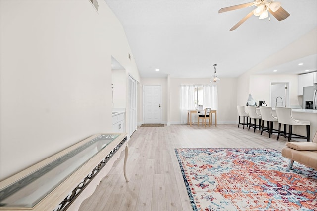 unfurnished living room featuring ceiling fan, vaulted ceiling, sink, and light wood-type flooring