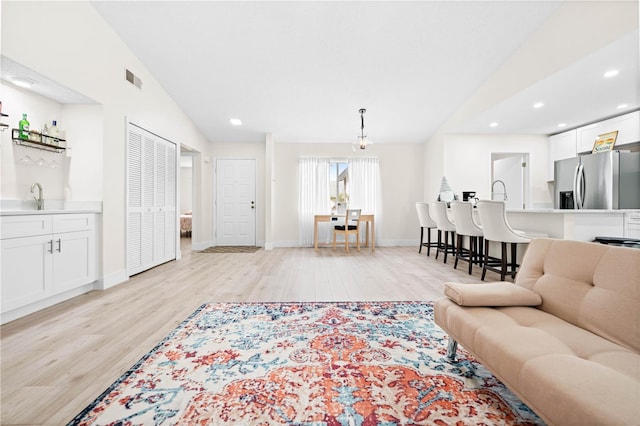 living room featuring lofted ceiling, wet bar, and light wood-type flooring