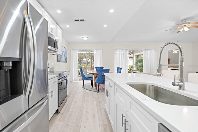 kitchen with sink, white cabinetry, stainless steel appliances, light stone counters, and light wood-type flooring