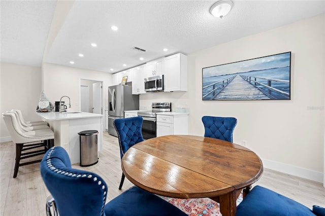 dining area featuring sink, light hardwood / wood-style floors, and a textured ceiling