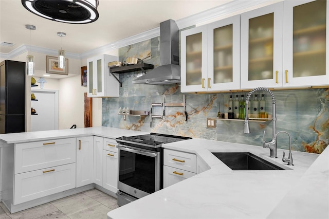 kitchen featuring electric range, a peninsula, wall chimney range hood, white cabinets, and a sink