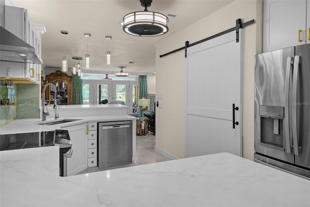 kitchen featuring light stone countertops, appliances with stainless steel finishes, a barn door, a sink, and a peninsula