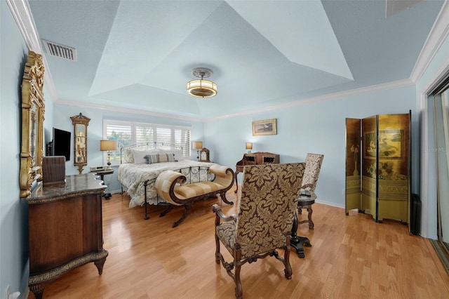 bedroom with light wood-style floors, crown molding, a tray ceiling, and visible vents