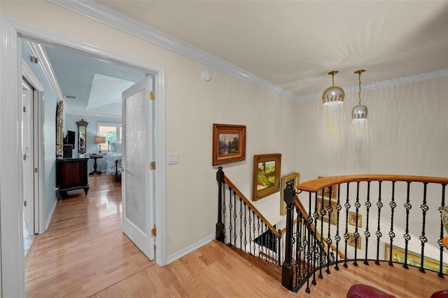 hall featuring light wood-style floors, baseboards, ornamental molding, and an upstairs landing