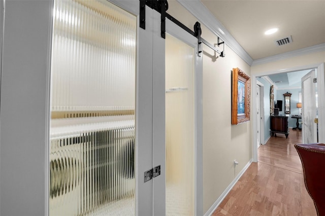 corridor with visible vents, ornamental molding, baseboards, light wood-type flooring, and a barn door
