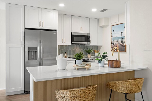 kitchen featuring light hardwood / wood-style flooring, a kitchen bar, stainless steel appliances, kitchen peninsula, and white cabinetry