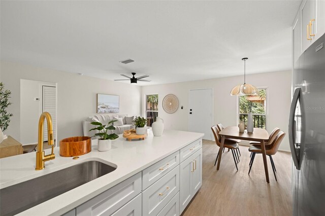 kitchen with decorative light fixtures, light hardwood / wood-style floors, white cabinetry, stainless steel refrigerator, and sink