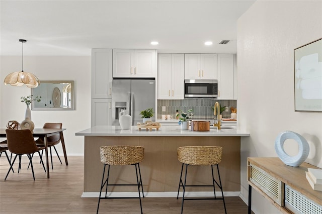 kitchen featuring pendant lighting, light hardwood / wood-style flooring, appliances with stainless steel finishes, decorative backsplash, and white cabinets