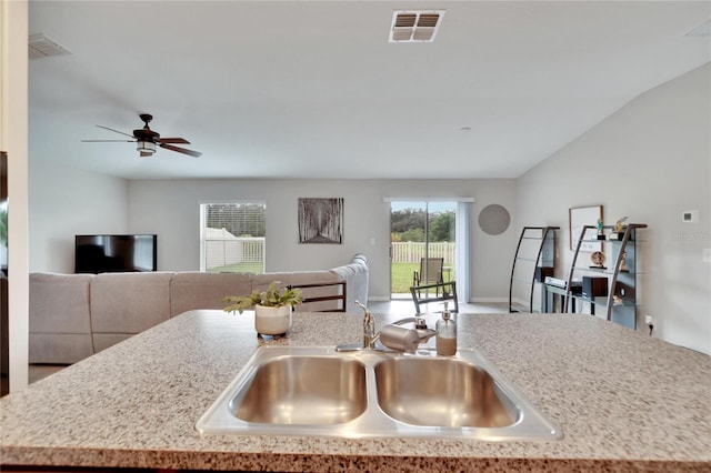 kitchen with vaulted ceiling, sink, a center island with sink, and ceiling fan