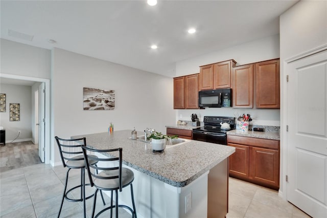 kitchen with a kitchen breakfast bar, black appliances, light stone counters, and an island with sink