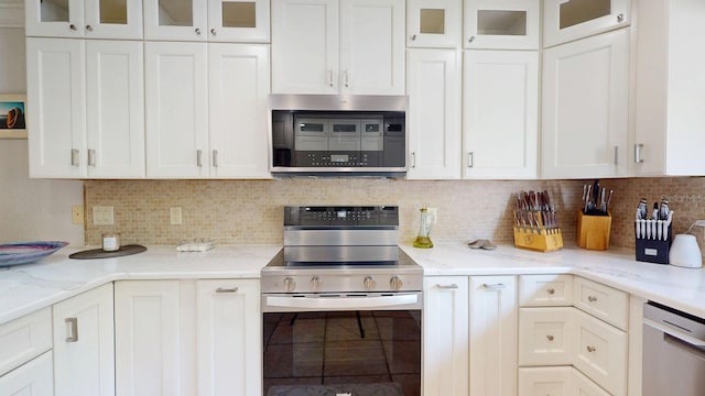 411 Harbor View Ln, Largo, FL 33770 - kitchen featuring appliances with stainless steel finishes, white cabinets, backsplash, light stone countertops, and glass insert cabinets