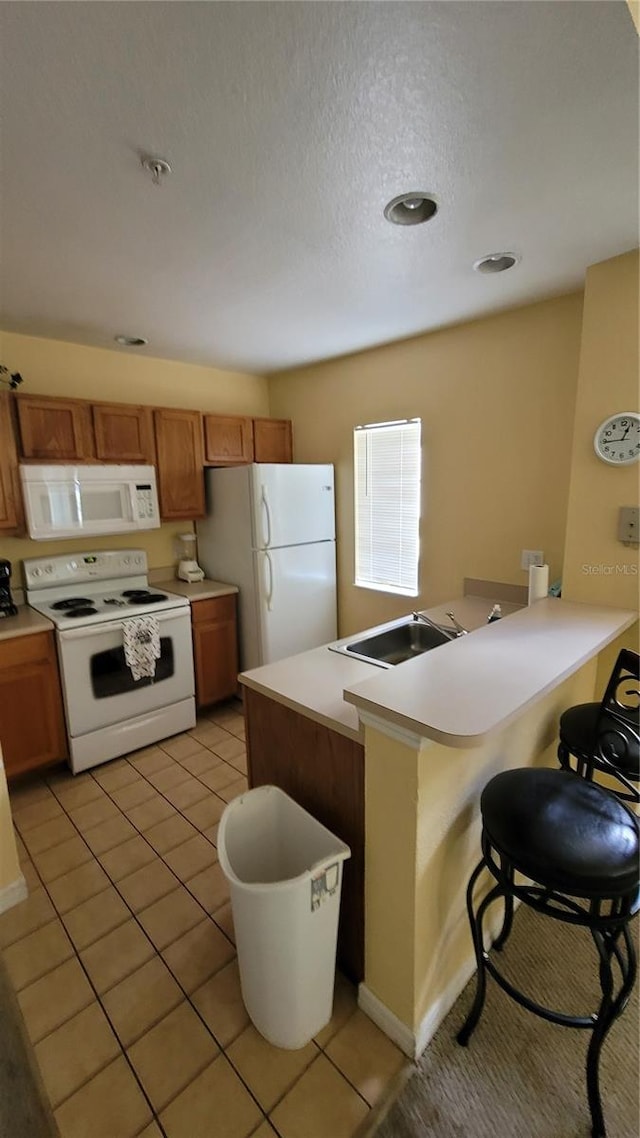 kitchen featuring light tile patterned floors, white appliances, sink, a breakfast bar, and a textured ceiling