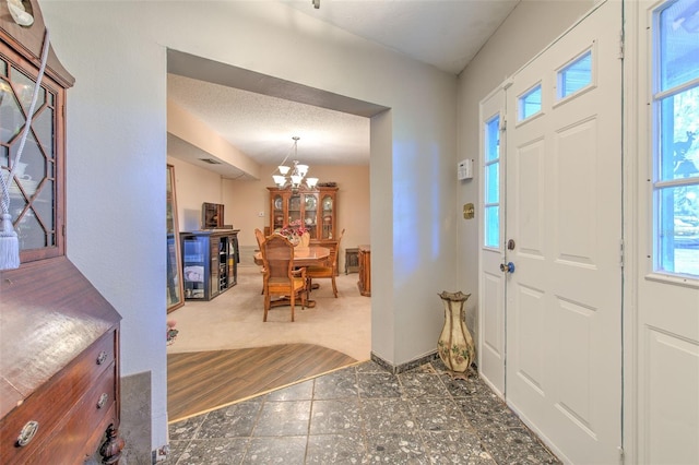 entrance foyer with a textured ceiling, plenty of natural light, dark wood-type flooring, and a chandelier