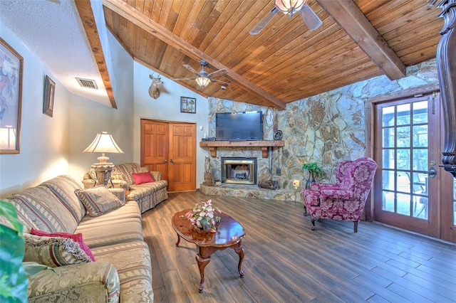 living room with ceiling fan, a stone fireplace, hardwood / wood-style flooring, and beamed ceiling