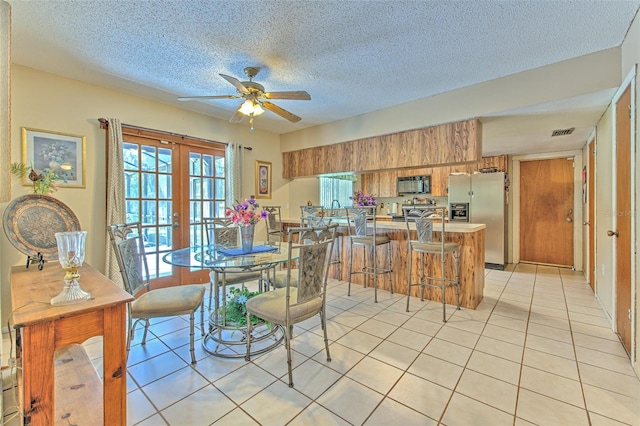 tiled dining space featuring ceiling fan, french doors, and a textured ceiling