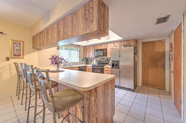 kitchen with light tile patterned floors, sink, kitchen peninsula, a textured ceiling, and black appliances