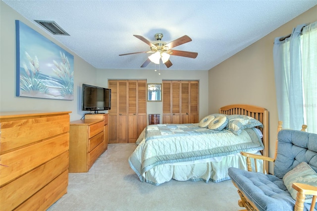 bedroom featuring ceiling fan, multiple closets, a textured ceiling, and light carpet