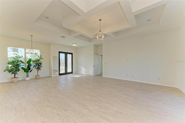 empty room featuring a chandelier, coffered ceiling, light hardwood / wood-style flooring, a raised ceiling, and french doors