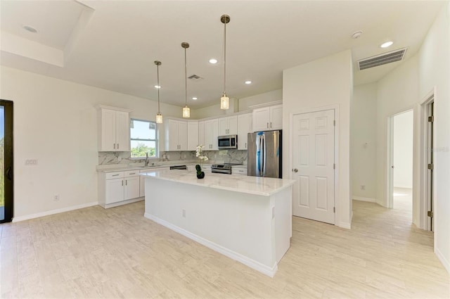 kitchen with sink, decorative light fixtures, white cabinetry, appliances with stainless steel finishes, and a center island