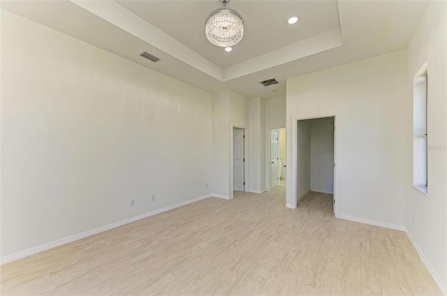 empty room with a raised ceiling, light hardwood / wood-style flooring, and a notable chandelier