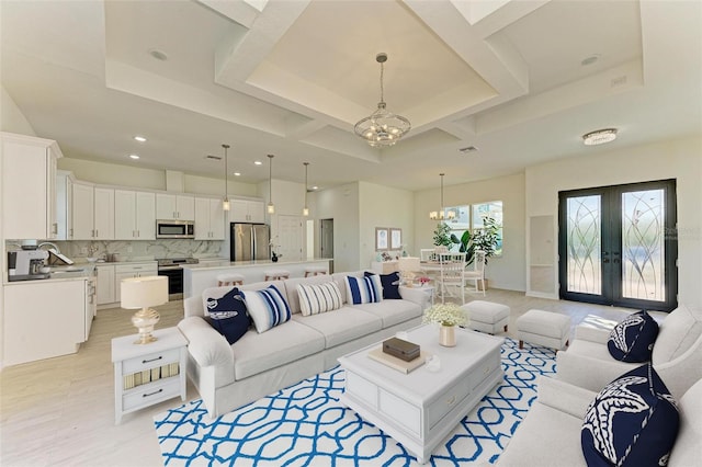 living room with coffered ceiling, light hardwood / wood-style flooring, a chandelier, and a tray ceiling