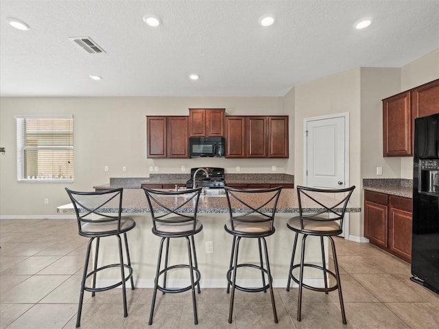 kitchen with black appliances, a kitchen island with sink, a kitchen breakfast bar, and a textured ceiling