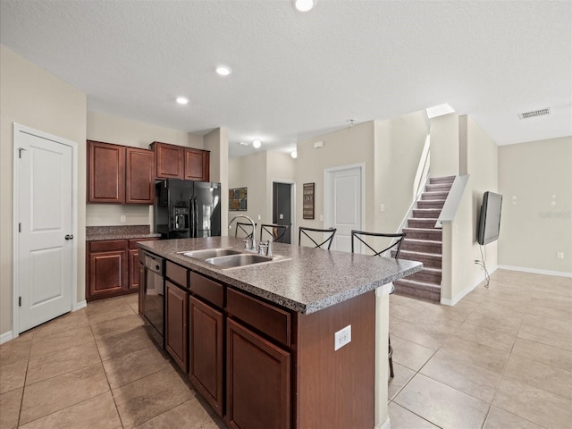 kitchen featuring black fridge, an island with sink, a kitchen bar, dishwasher, and sink