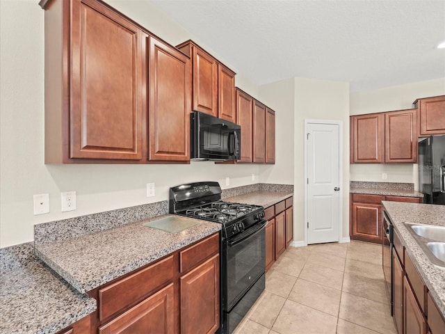 kitchen with light tile patterned flooring, black appliances, sink, and light stone counters