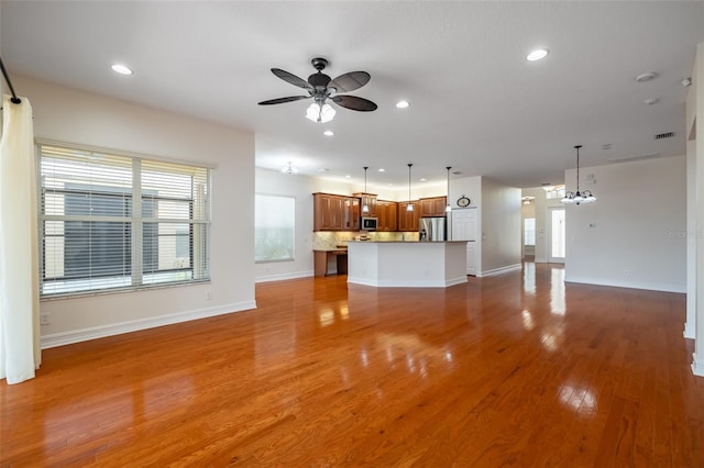 unfurnished living room featuring ceiling fan with notable chandelier and light wood-type flooring