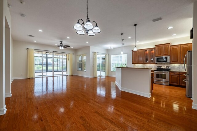 kitchen featuring brown cabinets, open floor plan, stainless steel appliances, ceiling fan with notable chandelier, and visible vents