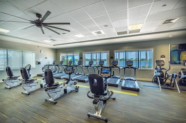 workout area featuring a paneled ceiling, ceiling fan, carpet floors, and brick wall