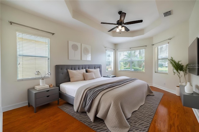 bedroom featuring ceiling fan, a raised ceiling, dark wood-type flooring, and multiple windows