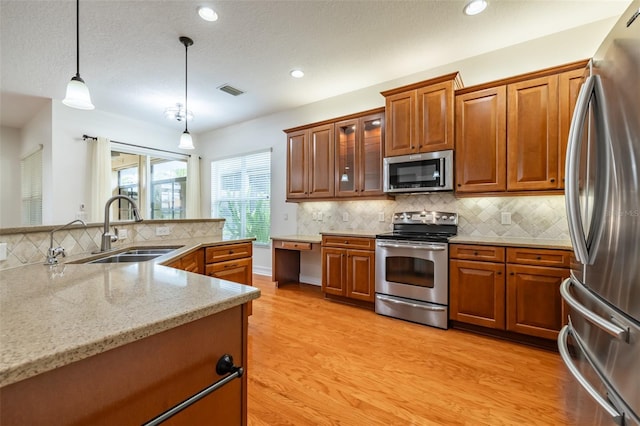 kitchen with sink, light stone counters, pendant lighting, light hardwood / wood-style floors, and appliances with stainless steel finishes